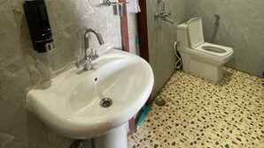 A bathroom with a pedestal sink, a mirror, a toilet, and a shower area.