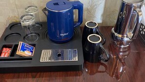 A coffee maker, two mugs, a kettle, and a small packet of coffee creamer on a wooden table.