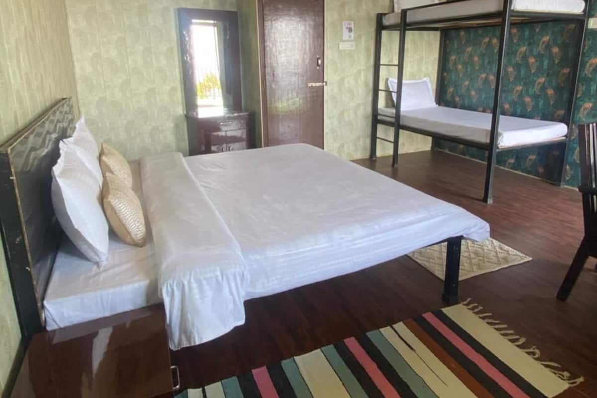 A hotel room with a bunk bed, a single bed, a wooden floor, and a striped rug.