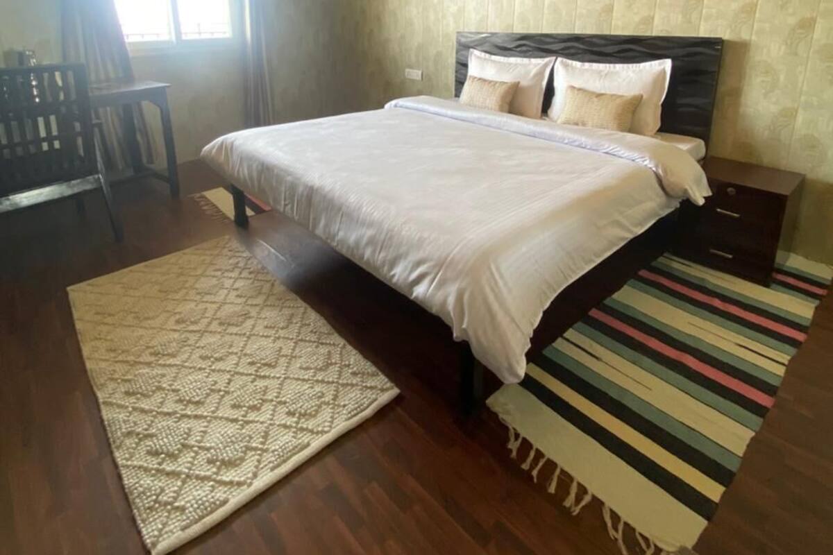 A bedroom with a bed, a nightstand, a chair, a window, and a patterned rug.