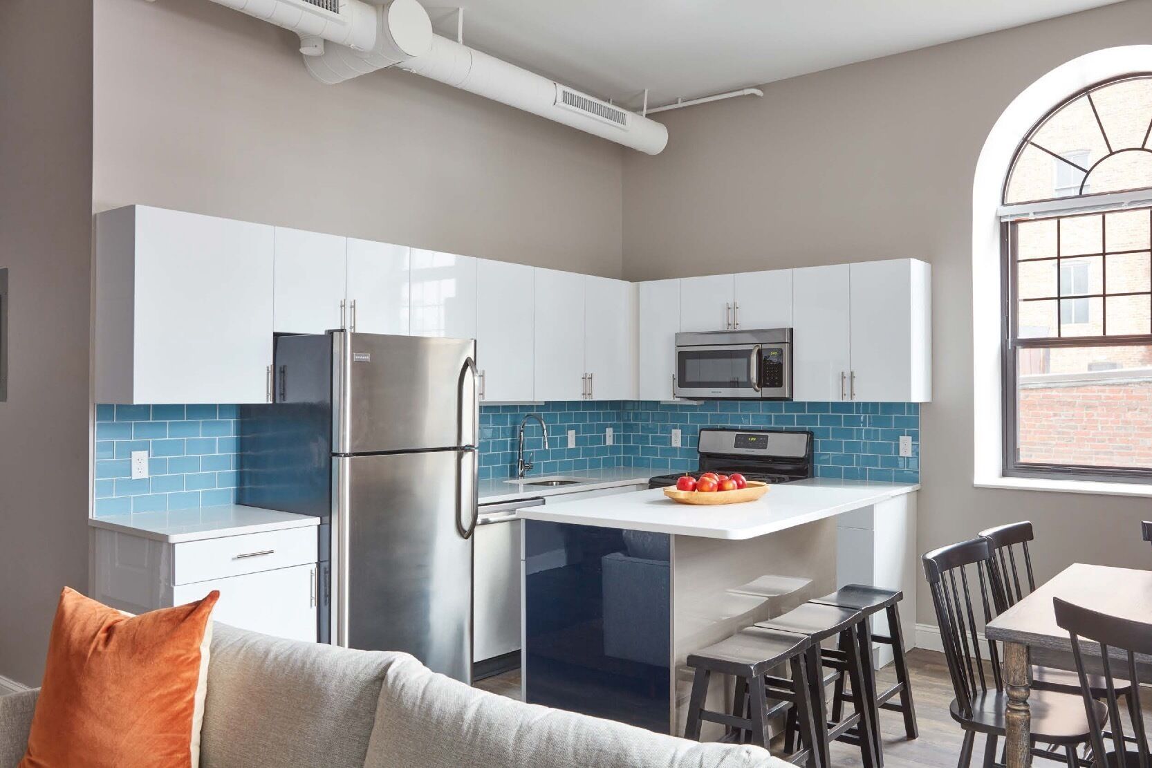 Een moderne keuken met witte kastjes, een roestvrijstalen koelkast, een magnetron en een blauwe tegelachterwand.