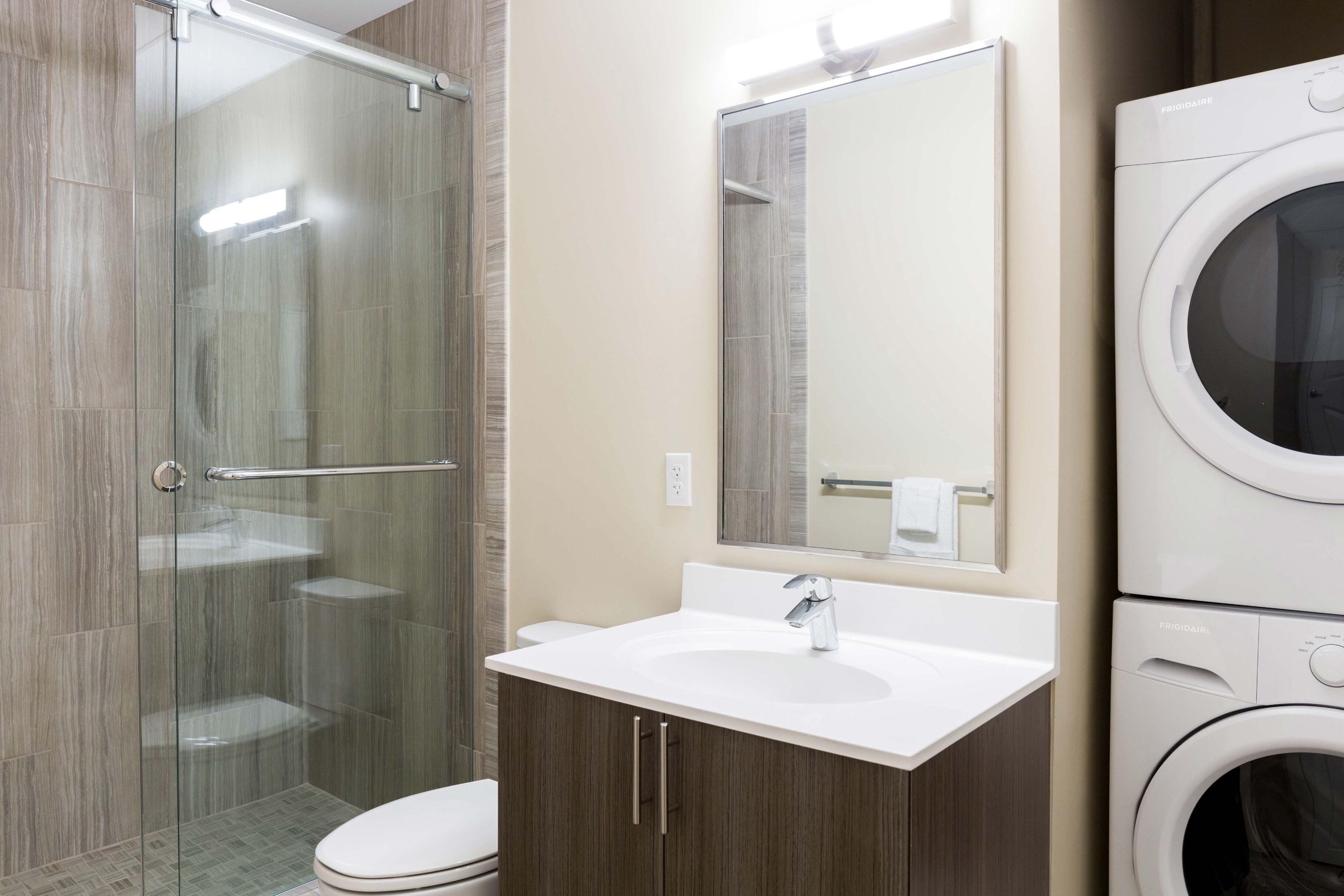 Un bagno moderno con box doccia in vetro, un lavandino bianco con specchio sopra e una lavatrice a carica frontale.