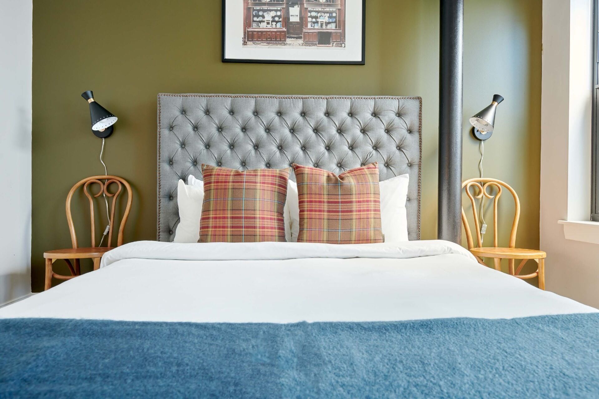A bed with a tufted headboard, two wooden nightstands, and a plaid pillow.