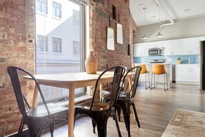 A dining area with a brick wall, a wooden table, and black chairs. - Kasa At Boston Common (Boston)