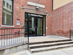 A brick building with a black door labeled '6 Hamilton Place.' There are security cameras and a 'No Trespassing' sign on the wall. - Kasa At Boston Common (Boston)