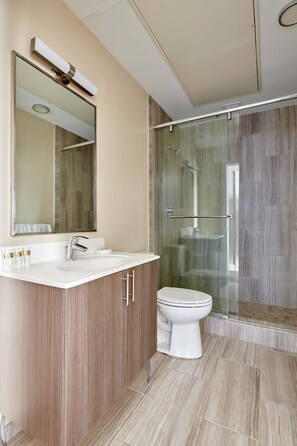 A modern bathroom with a glass shower enclosure, a large mirror, and a vanity with a sink and cabinet. - Kasa At Boston Common (Boston)