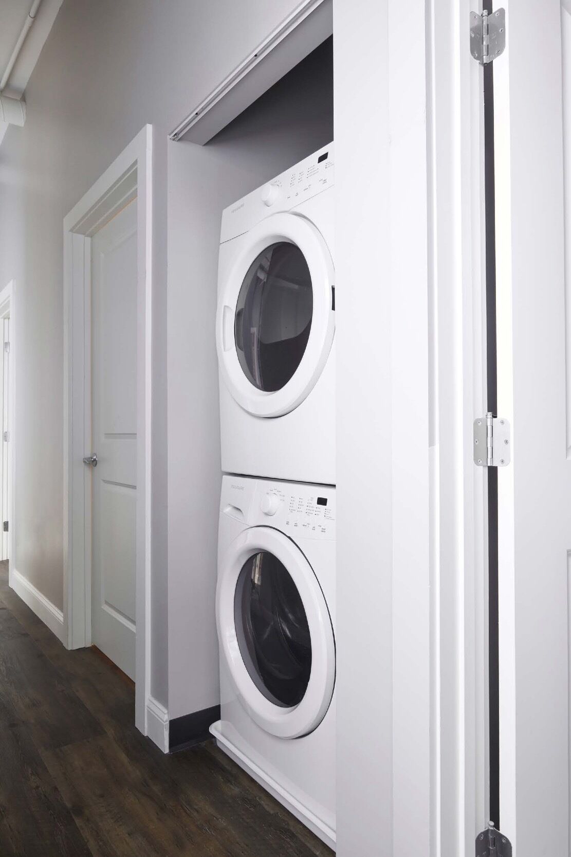 A laundry room with two white front-loading washing machines, a white door, and a wooden floor.