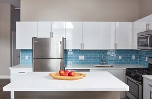 Cocina moderna con armarios blancos, refrigerador de acero inoxidable, microondas y salpicadero de azulejos azules.