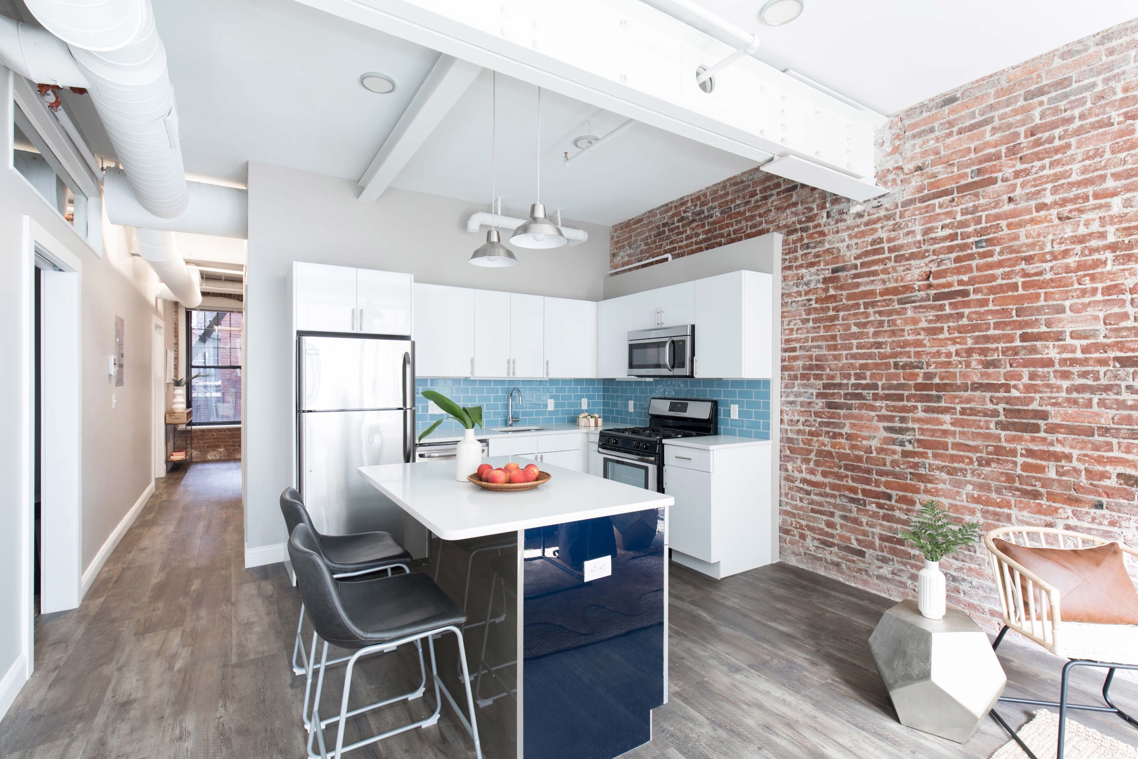 A modern kitchen with white cabinets, a blue backsplash, and a brick wall.