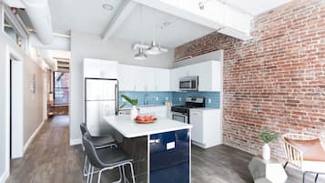 A modern kitchen with white cabinets, a blue backsplash, and a brick wall.