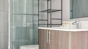 A modern bathroom with a glass shower enclosure, a white toilet, a vanity with a mirror, and a metal shelf unit.