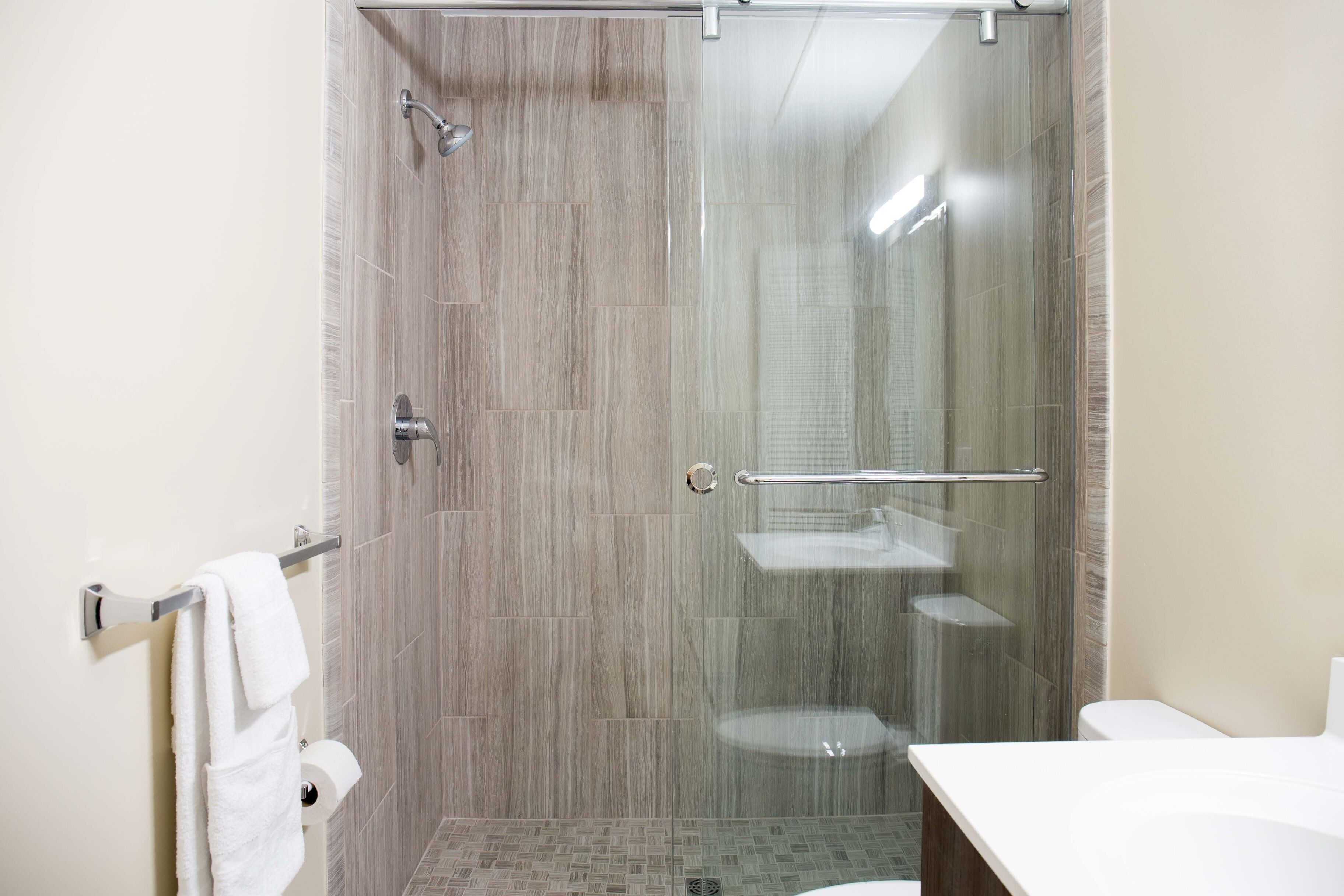 A modern bathroom with a glass-enclosed shower, a white sink, and a towel rack.