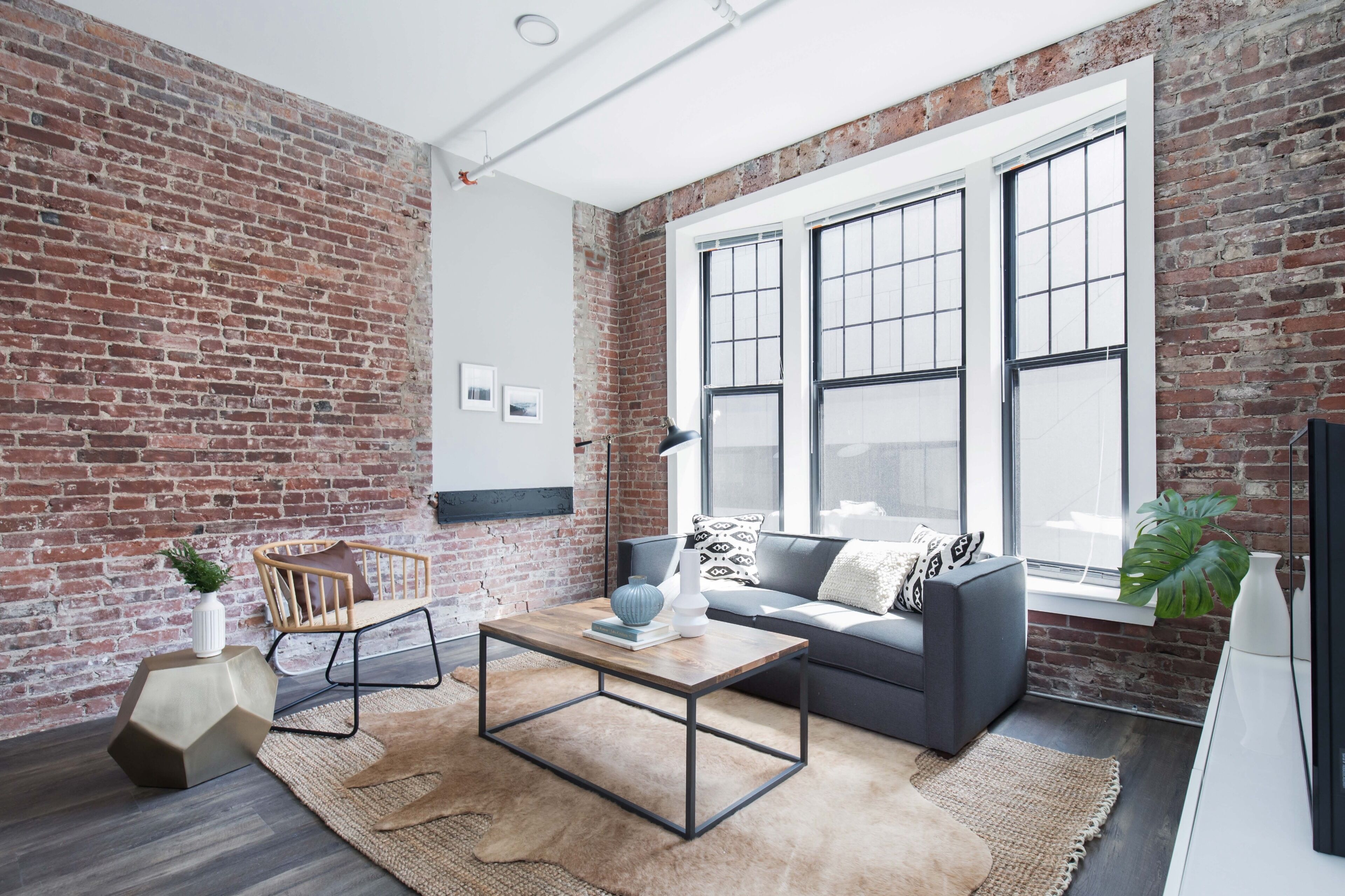 A modern living room with exposed brick walls, a large window, and a cozy seating area with a sofa and a coffee table.