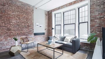 A modern living room with exposed brick walls, a large window, and a cozy seating area with a sofa and a coffee table.