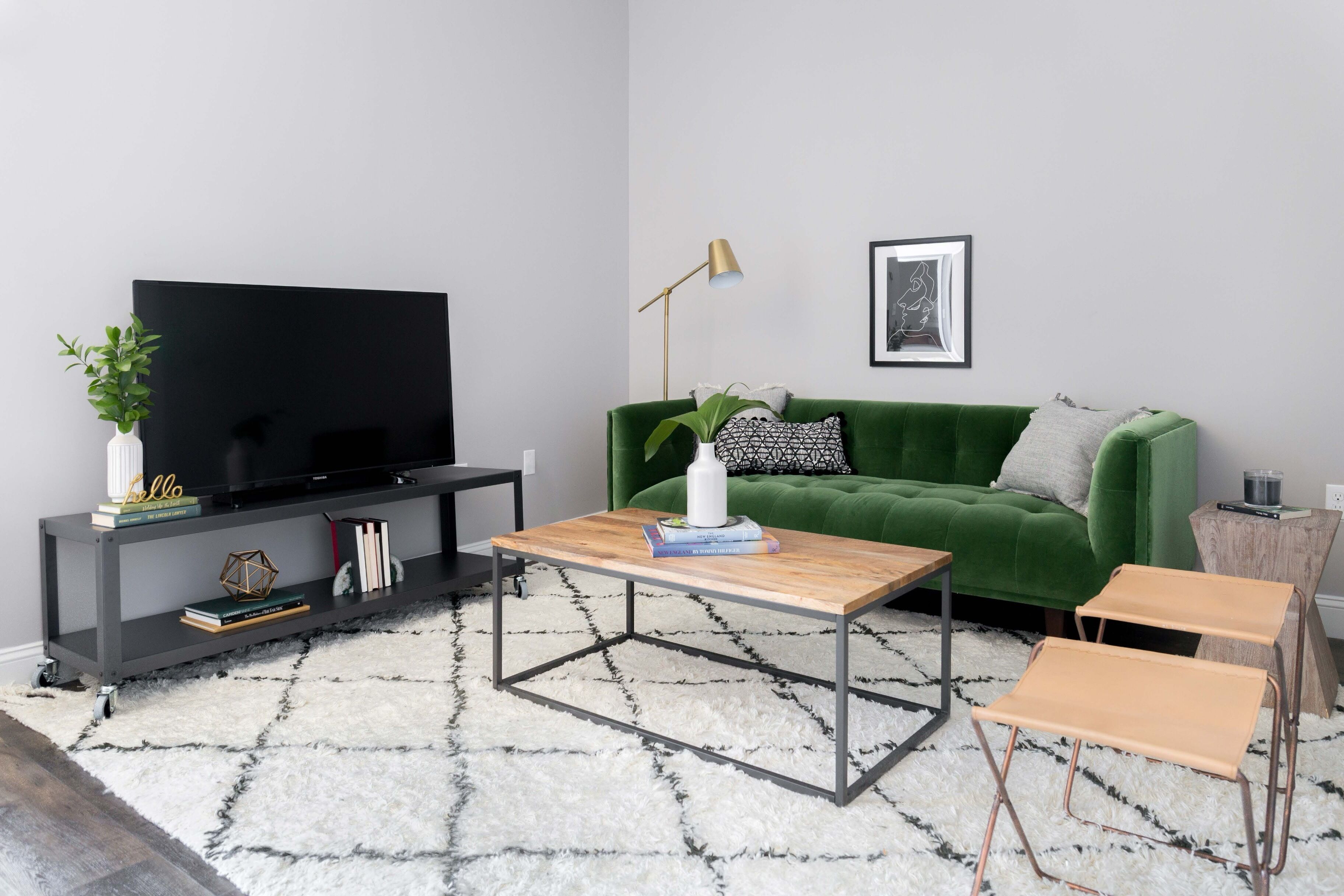 A modern living room with a flat-screen TV, a green sofa, a coffee table, and a small side table with a lamp.