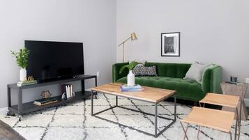 A modern living room with a flat-screen TV, a green sofa, a coffee table, and a small side table with a lamp.