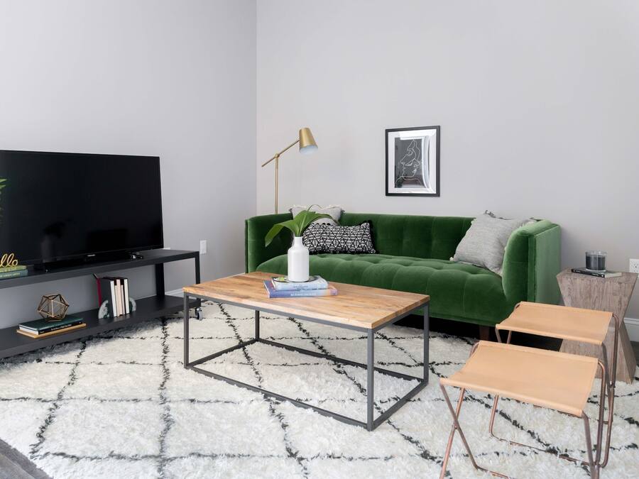 A modern living room with a flat-screen TV, a green sofa, a coffee table, and a small side table with a lamp.