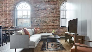 A living room with a brick wall, a sofa, a coffee table, a TV, and a dining area with chairs and a table.