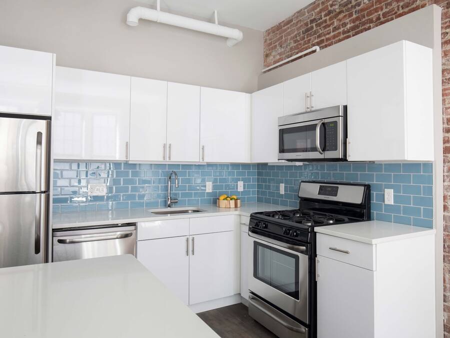 Una cocina moderna con electrodomésticos de acero inoxidable, armarios blancos y salpicadero de azulejos azules.