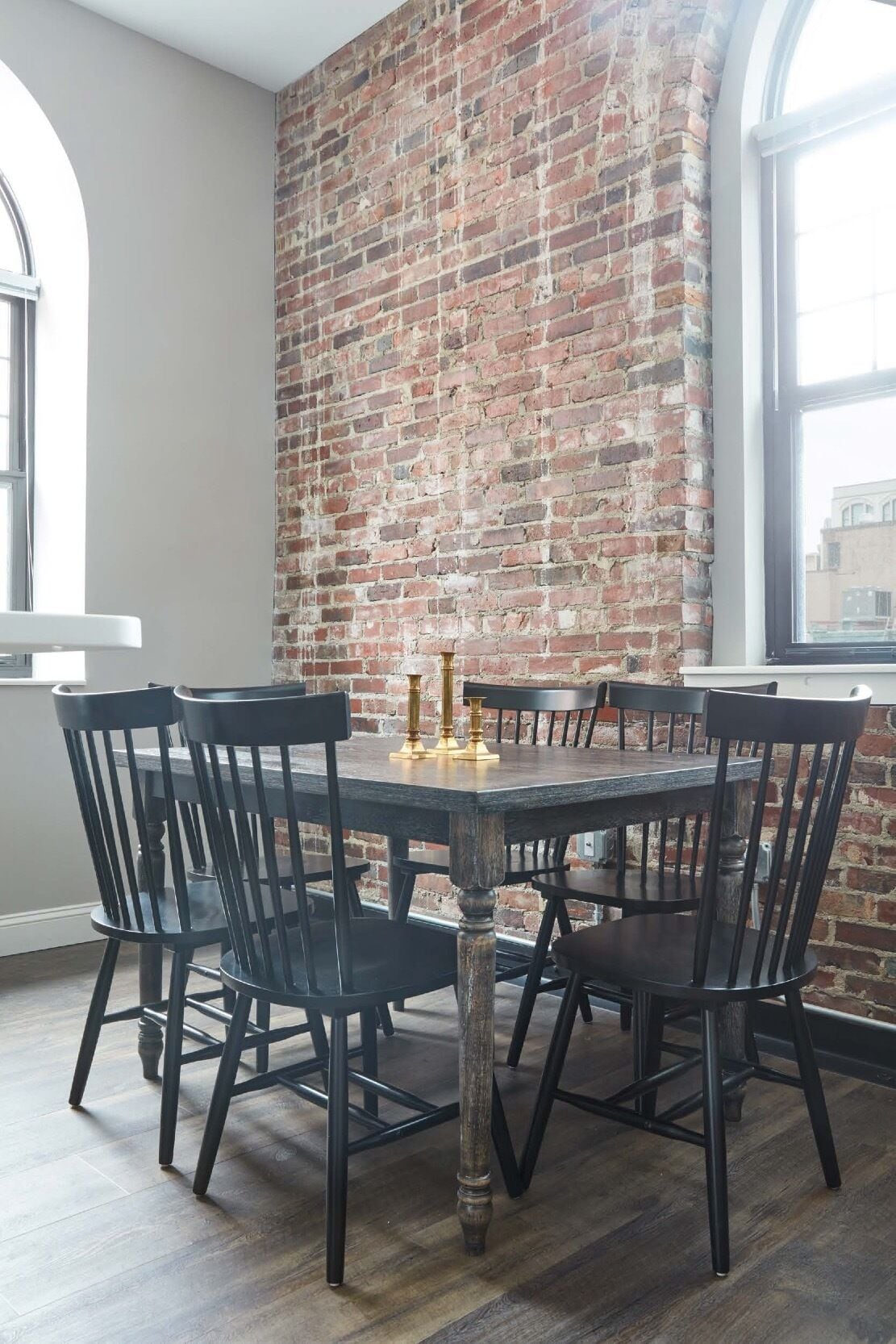 A dining area with a brick wall, a round table, and black chairs.