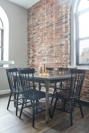 A dining area with a brick wall, a round table, and black chairs. - Kasa At Boston Common (Boston)