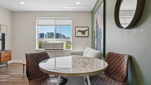 Un salon moderne avec une table ronde en marbre, des fauteuils en cuir, un canapé, un grand miroir et une vue sur la ville par la fenêtre.