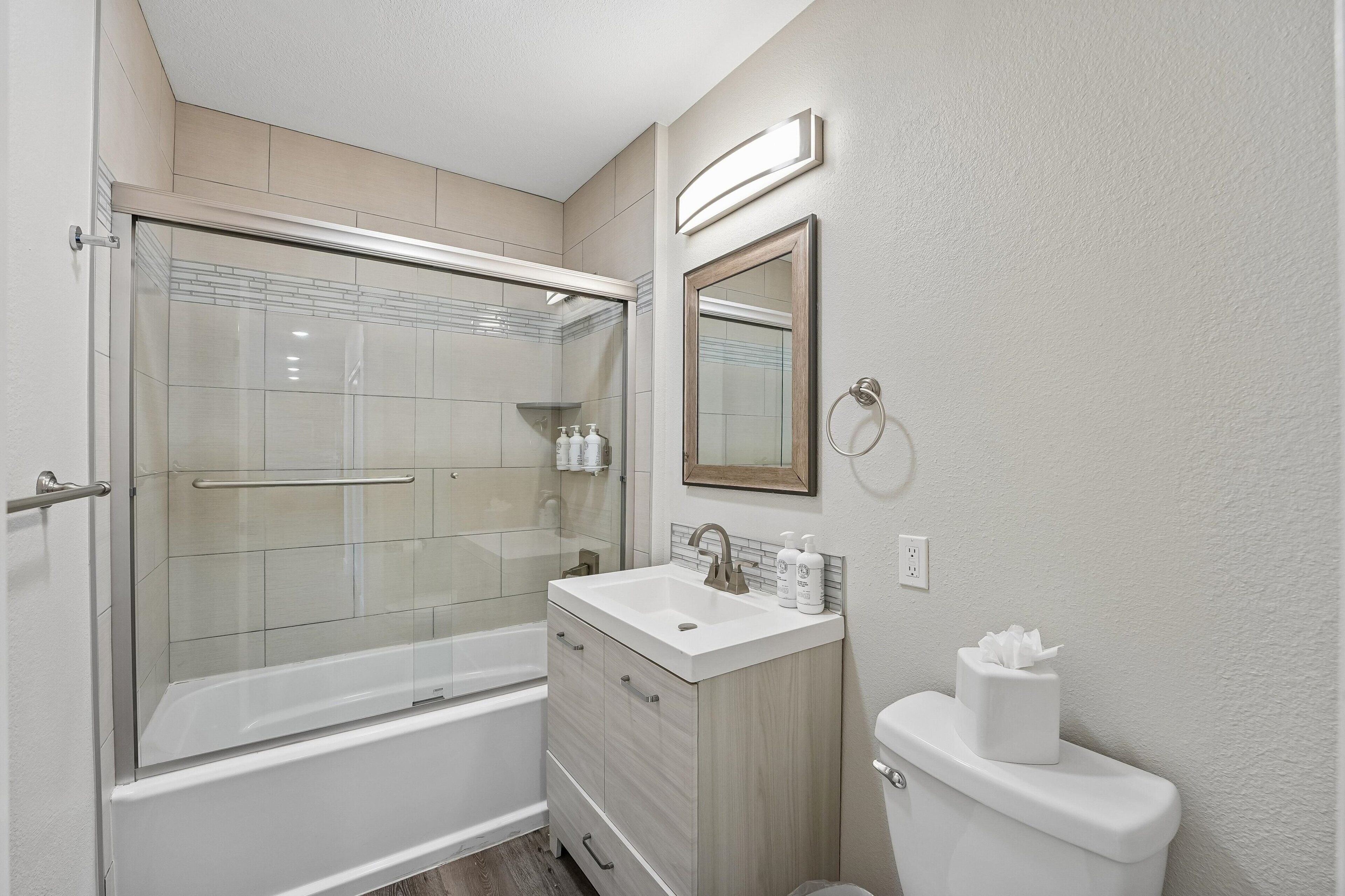 Un baño con ducha de vidrio, lavamanos blanco, tocador y retrete.
