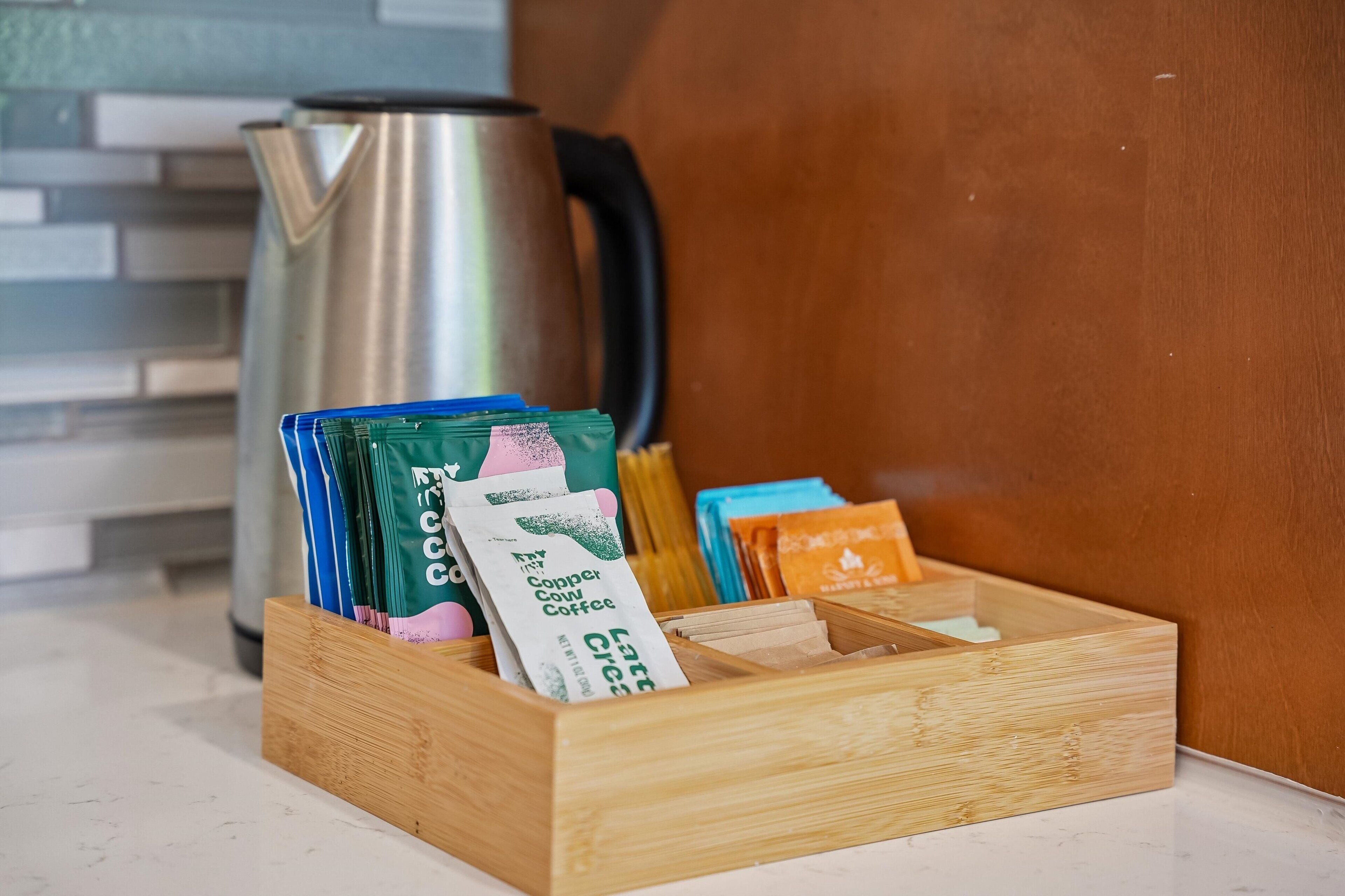 A wooden box with coffee packets and a kettle on a kitchen counter.