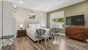 Une chambre à coucher comprenant un lit, des tables de chevet, un téléviseur, une commode et une fenêtre donnant sur un paysage agréable.