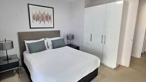 Une chambre à coucher avec un lit, des tables de chevet, une lampe, une armoire et un tableau encadré au mur.
