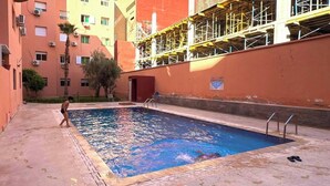 Ein Schwimmbecken mit Metallleiter, umgeben von einer Betonplattform, mit einem Gebäude im Hintergrund.