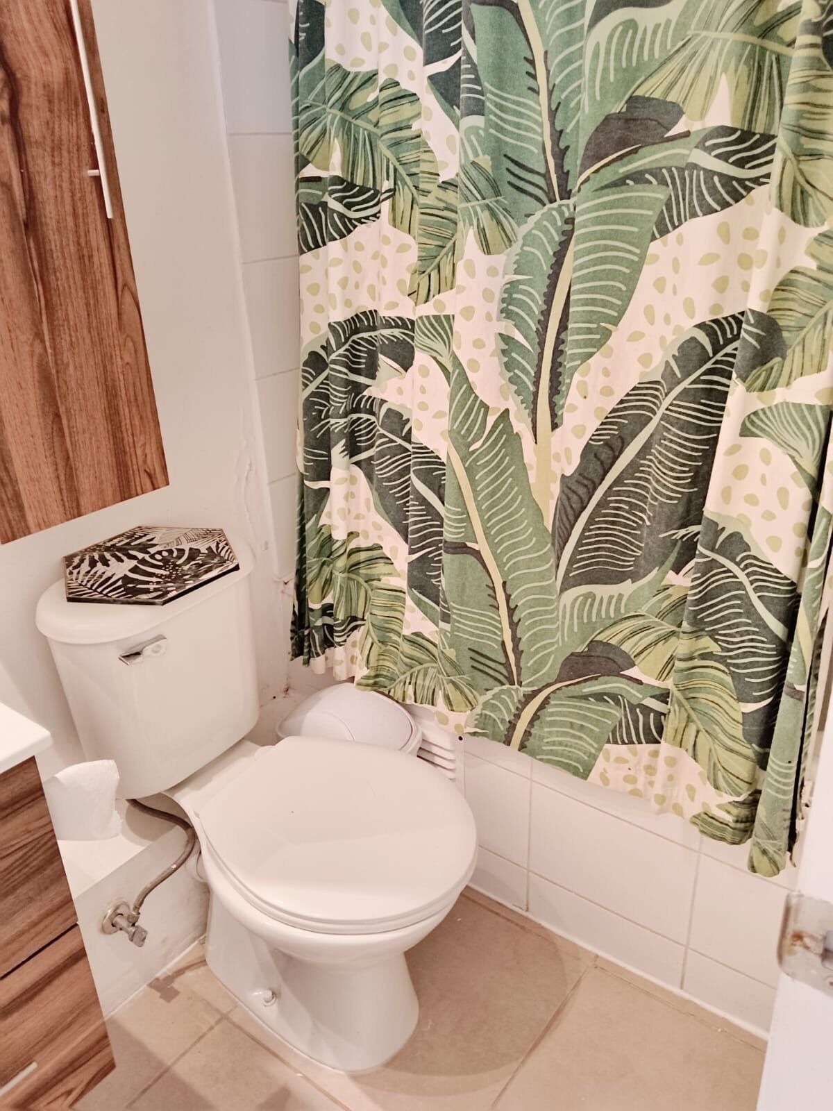 Un baño con inodoro, lavamanos y cortina de ducha con diseño de hojas.