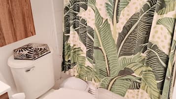 Un baño con inodoro, lavamanos y cortina de ducha con diseño de hojas.