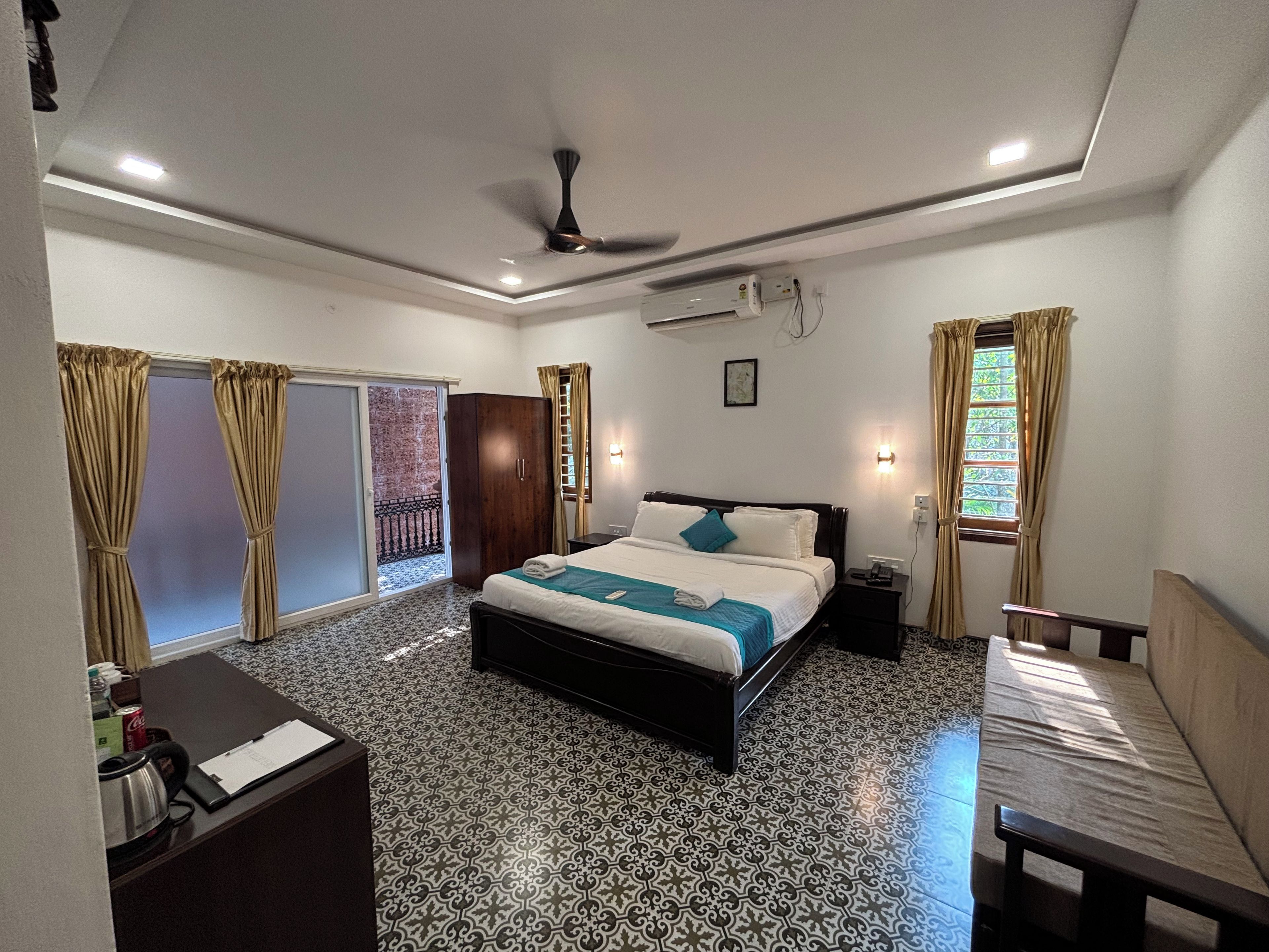 A hotel room with a bed, a desk, a wardrobe, a ceiling fan, and a window with curtains.