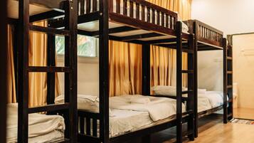 A bunk bed room with wooden frames, white bedding, and a window with curtains.