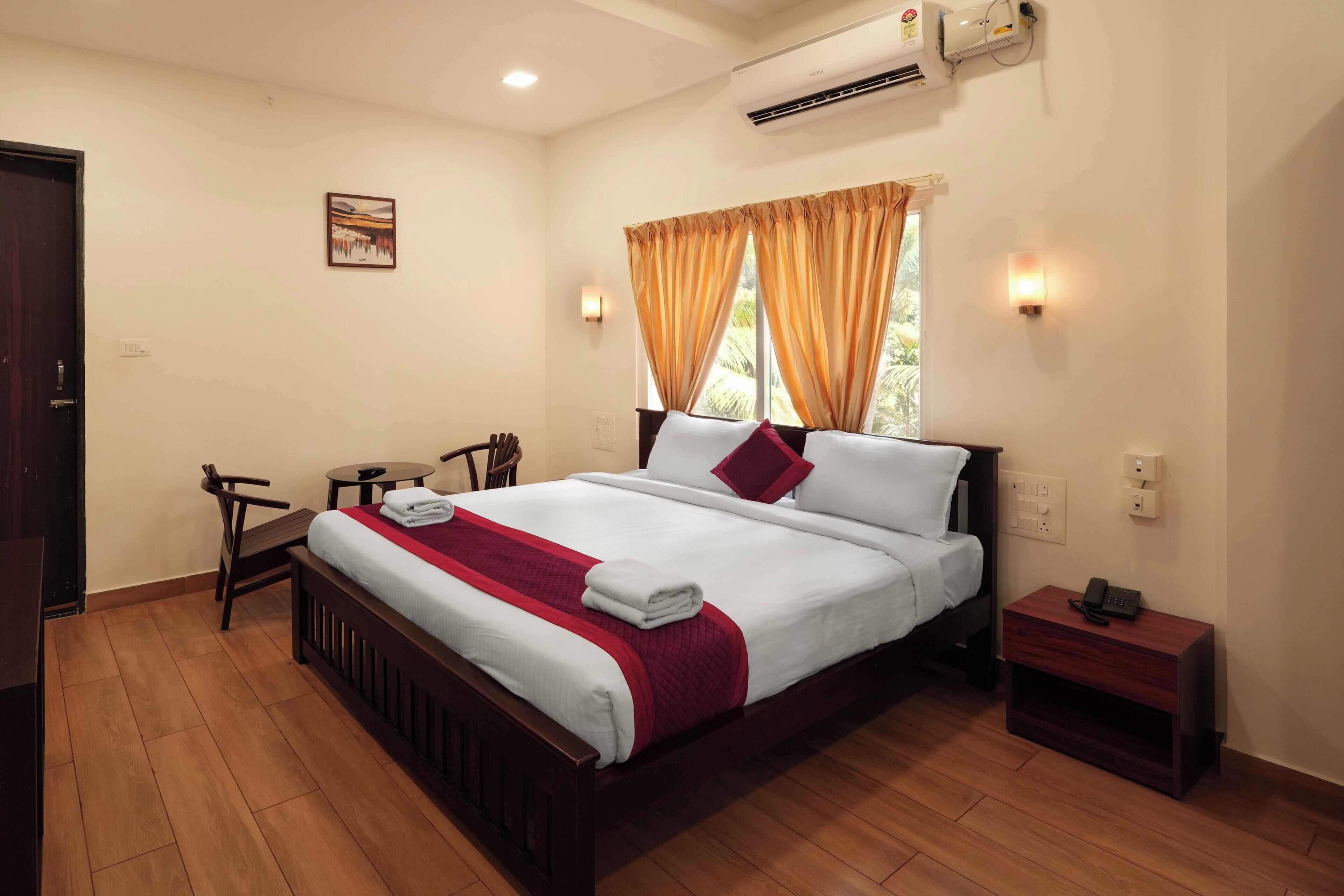 Une chambre d’hôtel équipée d’un lit, d’un bureau, d’une chaise, d’un climatiseur et d’une fenêtre avec des rideaux.
