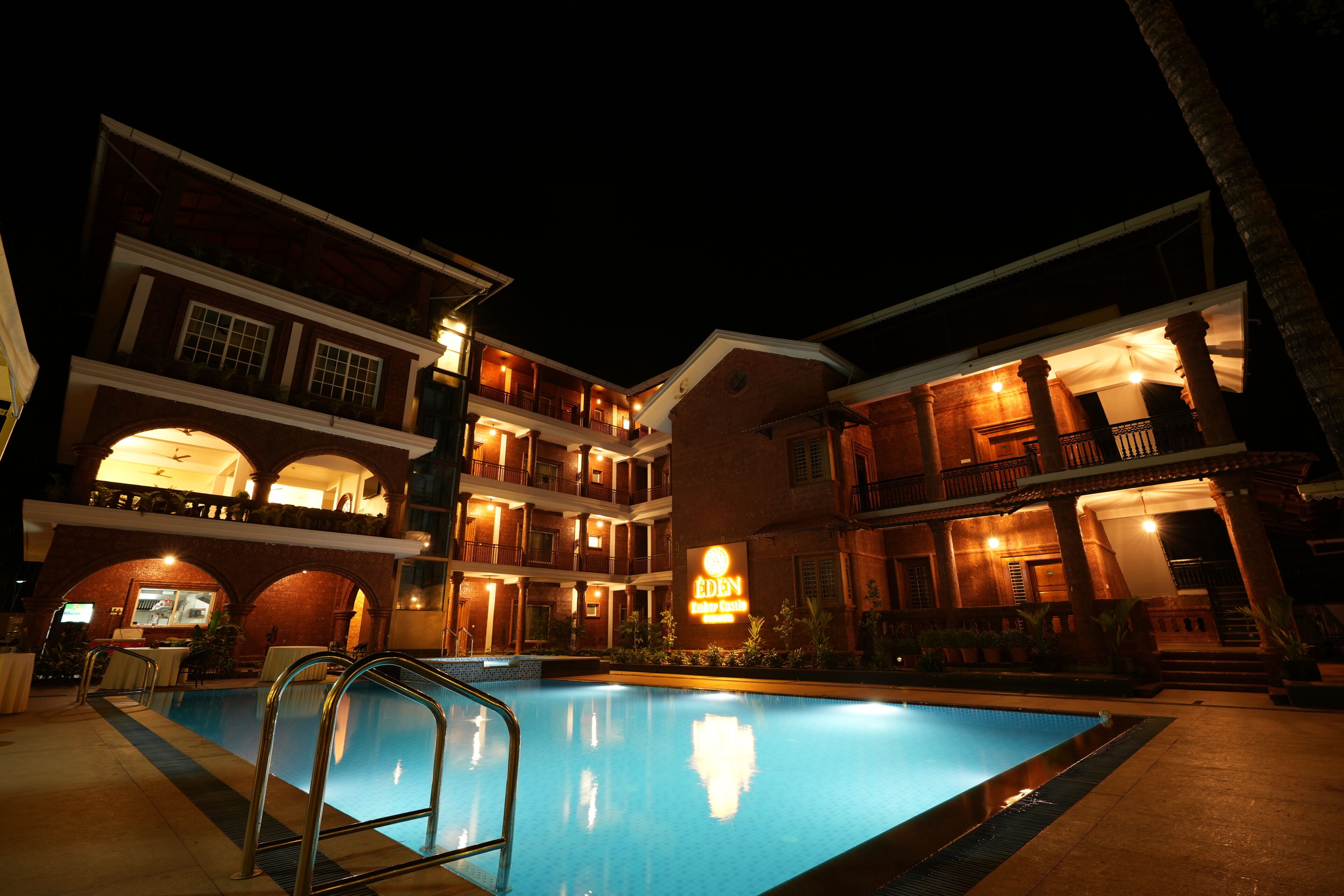 A hotel with a swimming pool, multiple balconies, and a sign indicating the name 'Eden Beach Resort.'