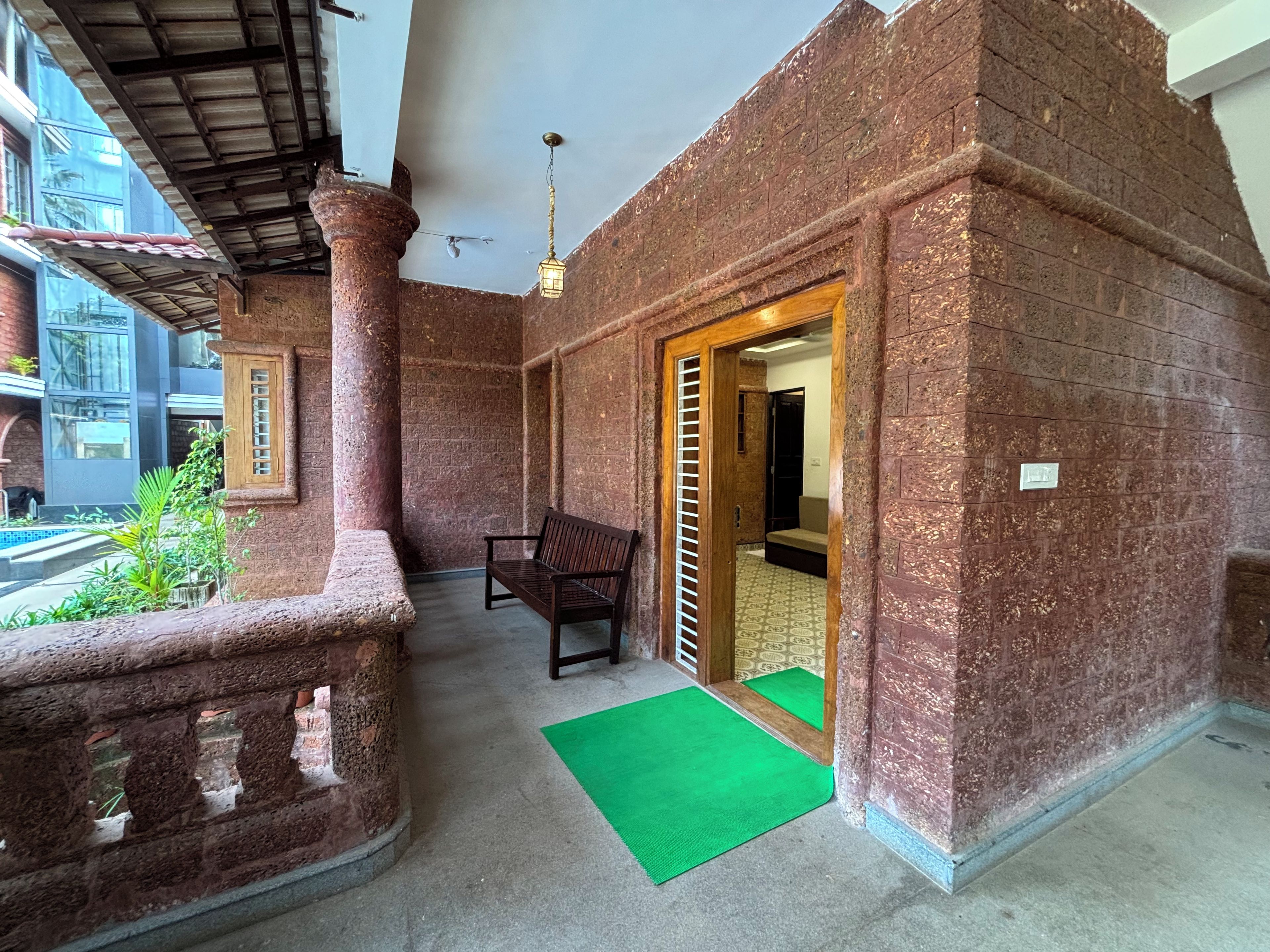 A balcony with a wooden bench, a green mat, and a view of a building with a tiled roof.