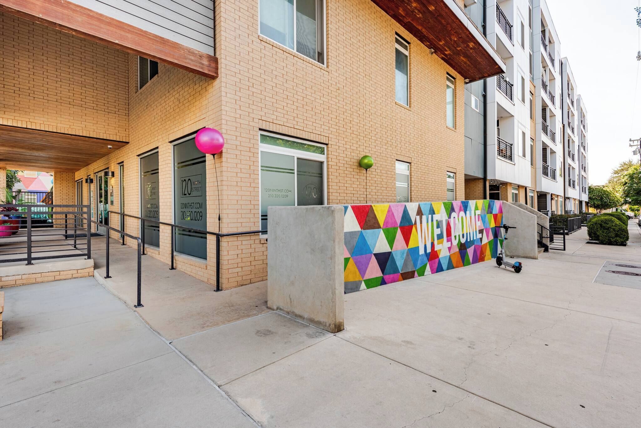 A multi-story building with a brick facade, a colorful geometric wall, and a scooter parked outside.