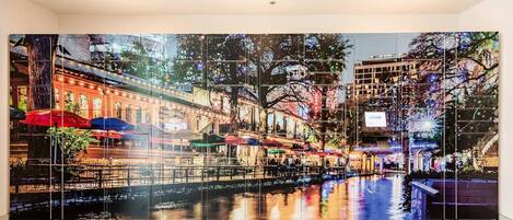 Una obra de arte mural grande y reflectante que muestra un paisaje urbano nocturno con edificios y árboles.