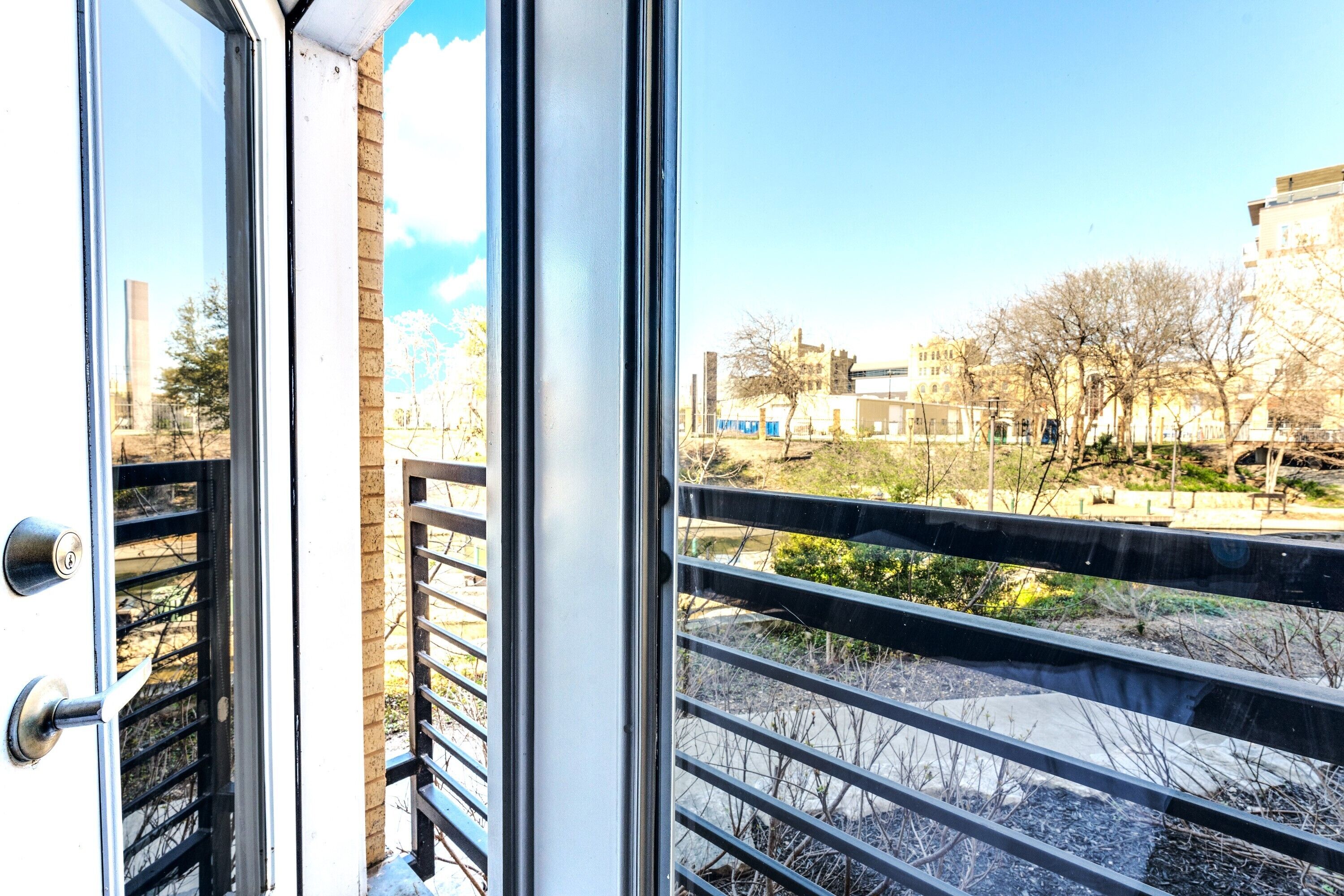 A view through a window with a metal railing, a door with a keyhole, and a clear sky.