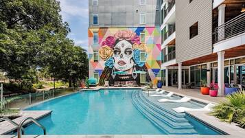 Una piscina con un mural en el edificio contiguo, rodeada de vegetación y arquitectura moderna.