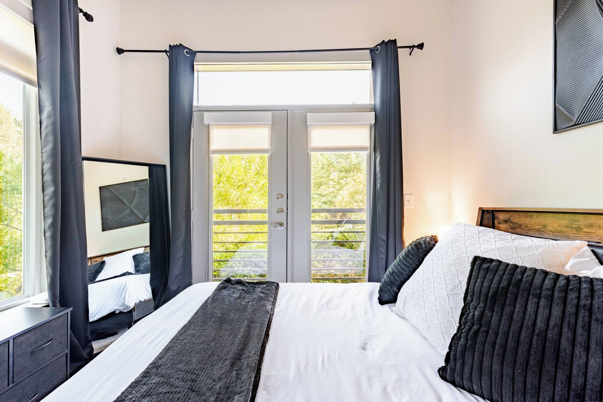A bedroom with a bed, curtains, a window, and a view of greenery.