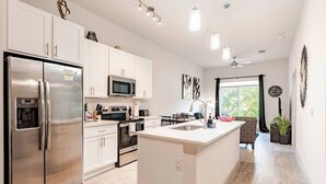 A modern kitchen with stainless steel appliances, a central island, and a dining area with a view. - Riverwalk Oasis - Pool, Free Parking & Views (San Antonio)