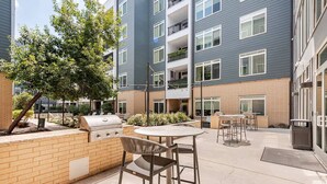 An outdoor patio area with a grill, chairs, and a table. - Riverwalk Oasis - Pool, Free Parking & Views (San Antonio)