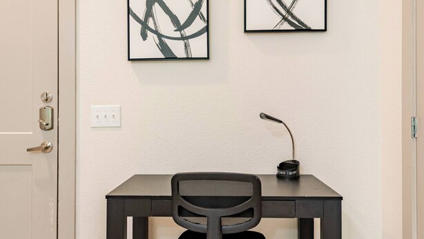 A room with a desk, two abstract paintings, a chair, and a door. - Riverwalk Oasis - Pool, Free Parking & Views (San Antonio)