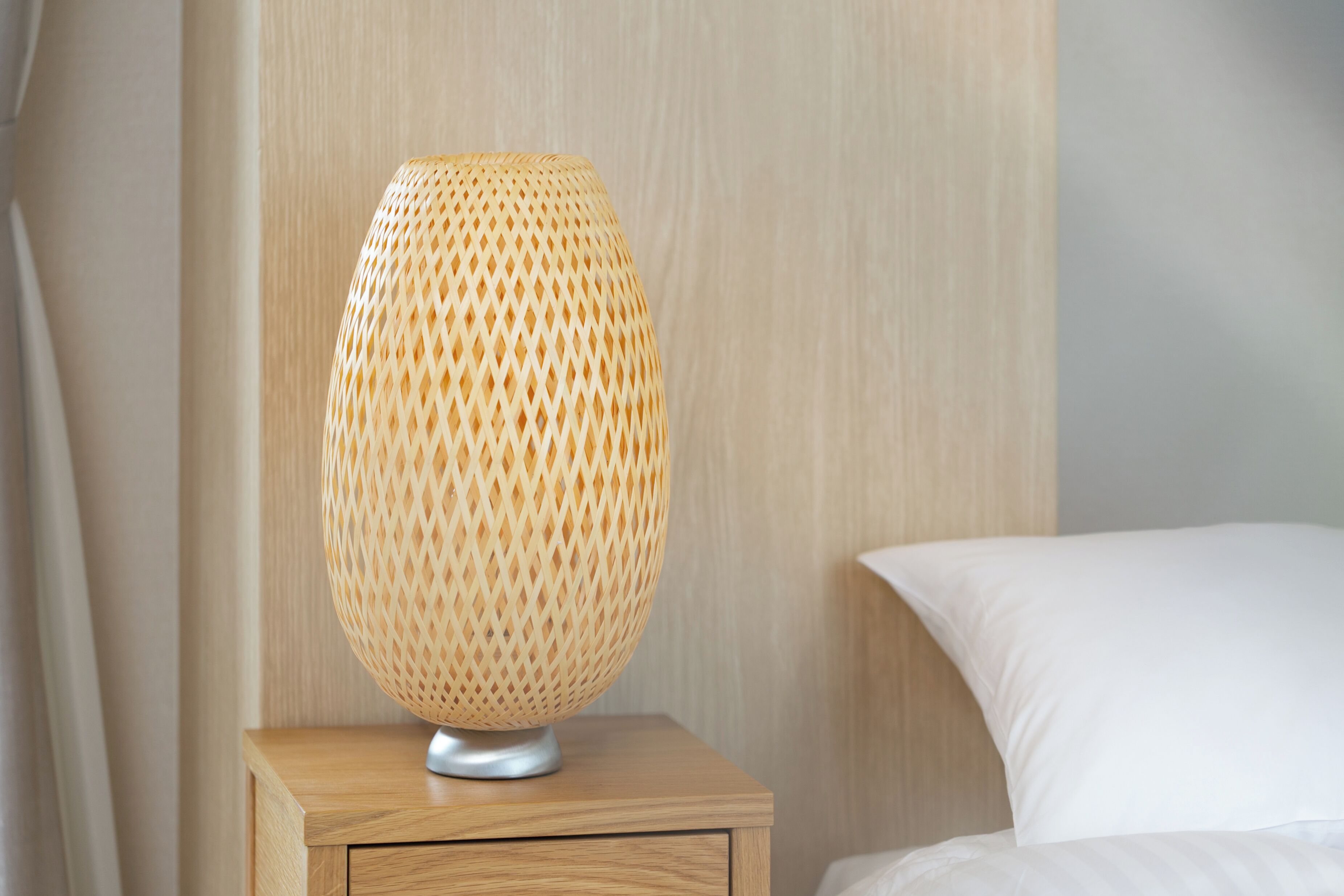 A lamp on a wooden bedside table next to a bed with a white pillow.