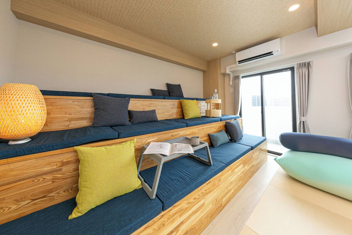 A modern living area with a sofa, cushions, a table with a book, and an air conditioning unit.