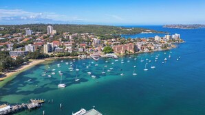Un pueblo costero con un puerto deportivo lleno de barcos, rodeado de edificios residenciales y un cielo azul despejado.