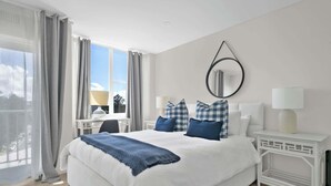 Habitación de hotel con una cama grande, una mesita de noche con lámpara, una silla y vistas al exterior.